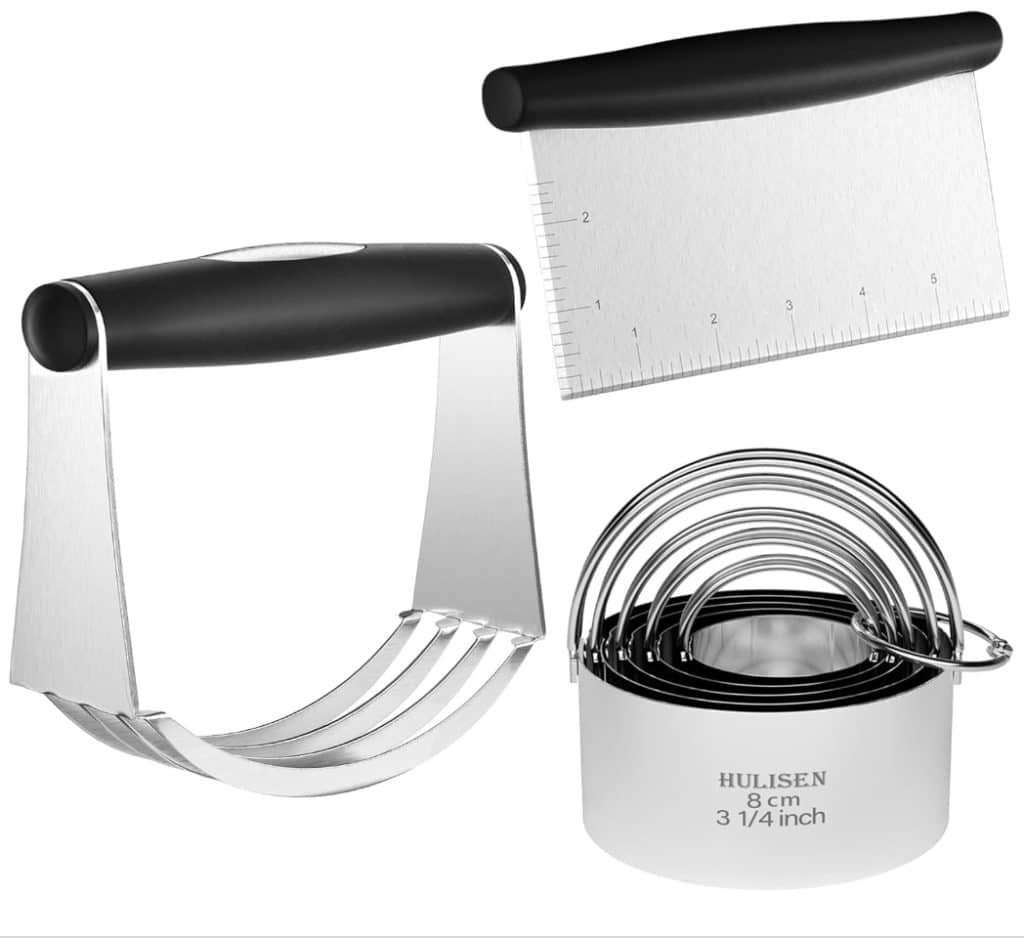 A stainless steel baking tool set ideal for perfecting your Costco Pumpkin Pie Recipe, featuring a dough cutter with a black handle, a bench scraper with measurement markings, and a round biscuit cutter set in varying sizes.